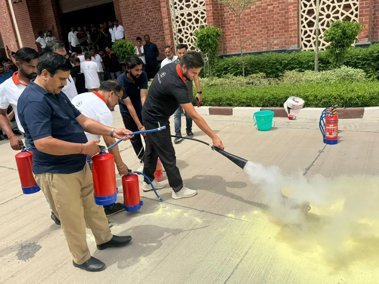 Employees discharging red ABC dry powder fire extinguishers onto a practice fire during hands-on fire safety training