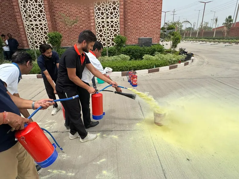 Line of trainees operating ABC dry powder extinguishers together, yellow powder discharging across the ground