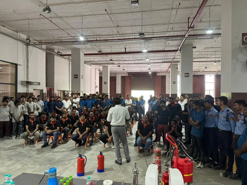 Fire safety training session inside a warehouse, staff seated in front of an instructor with CO2, foam and dry powder extinguishers displayed