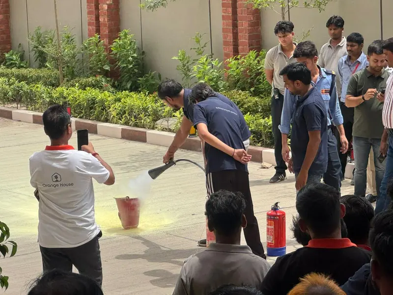 Trainee extinguishing a demonstration fire with a CO2 extinguisher horn while colleagues and security staff observe