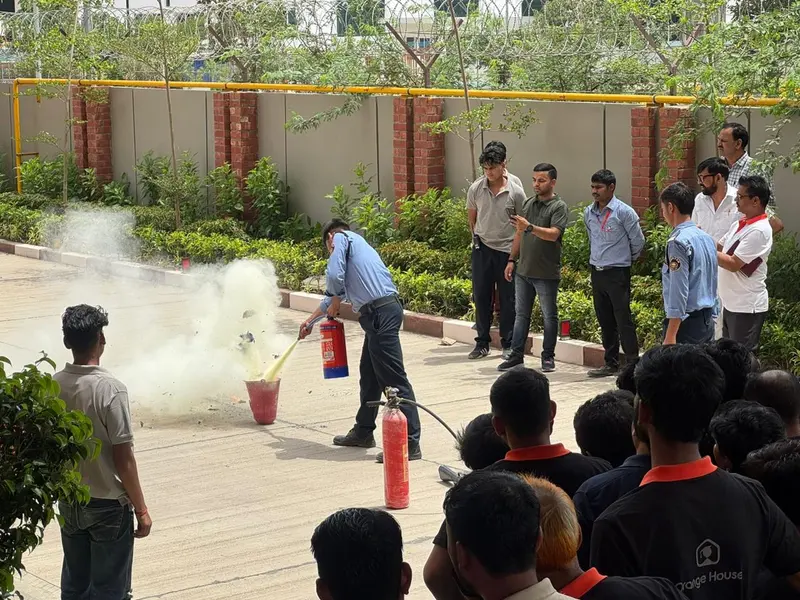 Trainer knocking down a live practice fire in a tray with a dry powder extinguisher while staff watch from a safe distance