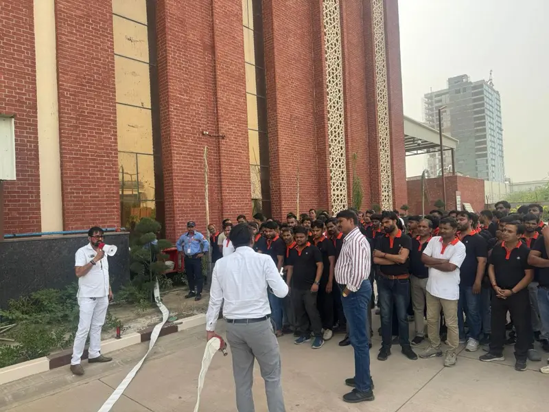 Fire safety trainer holding a fire hose nozzle while demonstrating hose handling to assembled factory employees