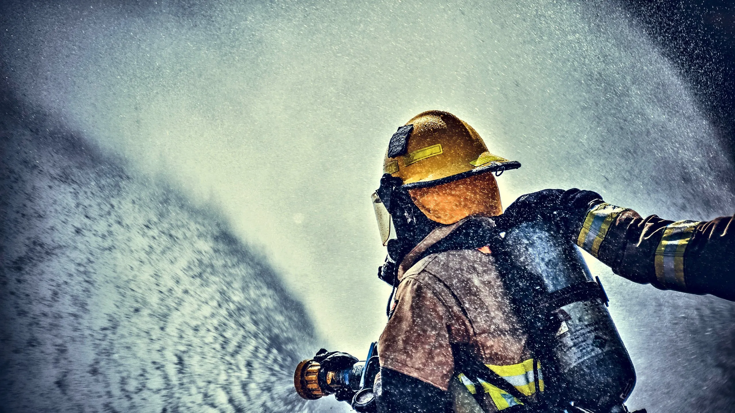 Firefighter in breathing apparatus and helmet directing a high-pressure water spray from a hose nozzle